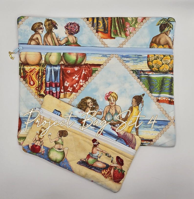 May include: Two rectangular fabric zipper pouches featuring a quilted texture and a colorful beach scene print. The design displays various figures relaxing on a sandy shore with blue water and sky. The text Project Bag Set 4 is printed in white.