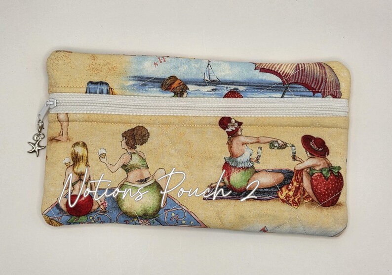 May include: A rectangular fabric pouch with a white zipper and a silver starfish charm. The pouch features a beach scene print with people, umbrellas, and strawberries, and the text Notions Pouch 2 printed in white script across the center.