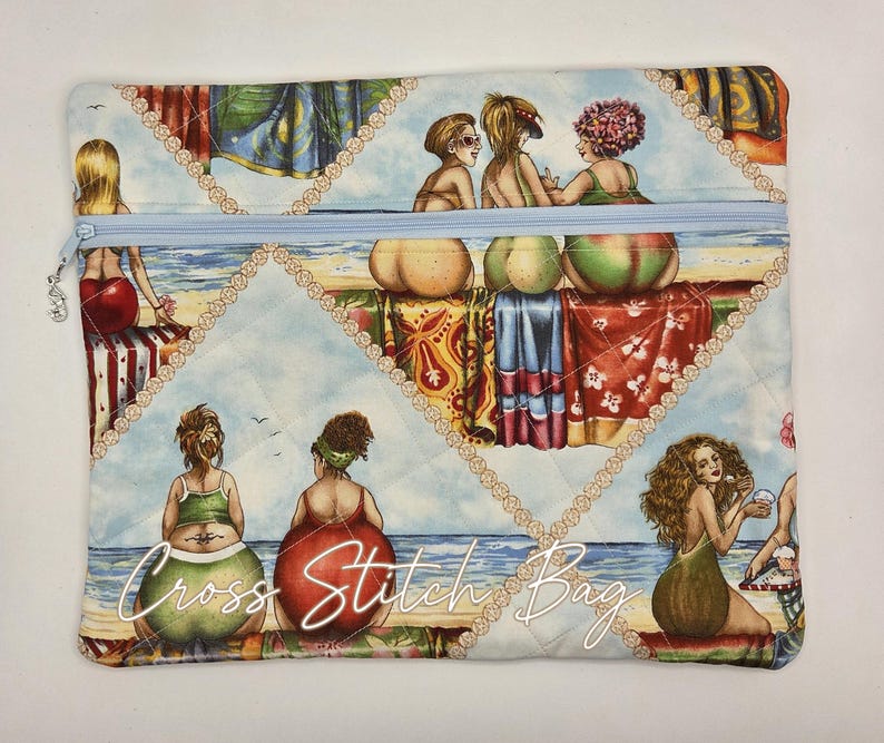 May include: A rectangular quilted fabric pouch with a light blue zipper closure. The surface features a colorful beach scene print with multiple figures sitting on towels by the ocean. The text Cross Stitch Bag is printed in white script.