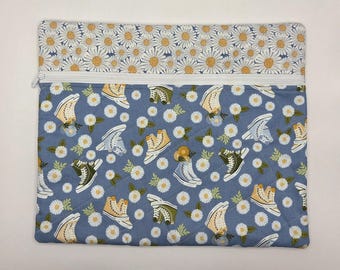 May include: A rectangular quilted zipper pouch featuring a top band of white daisy flowers on a light background. The main body is a dusty blue fabric patterned with white daisies and various high-top sneakers in yellow, olive, and light blue.