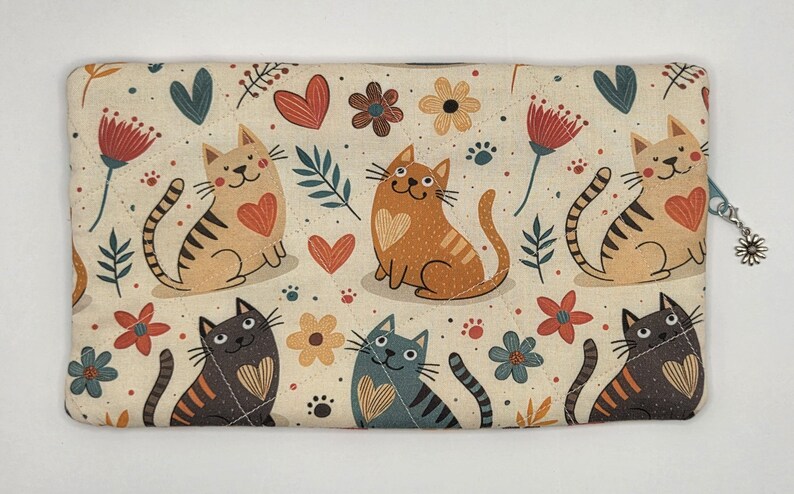 May include: A rectangular quilted fabric pouch featuring a repeating pattern of cats in shades of tan, gray, and black, interspersed with red hearts, colorful flowers, and green leaves on a cream background, finished with a silver daisy zipper pull.