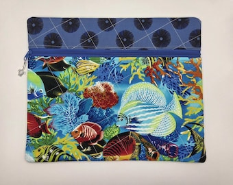 May include: A rectangular fabric zipper pouch featuring a vibrant underwater coral reef scene with various colorful tropical fish. The top section is a solid blue fabric with a dark circular pattern. A small silver turtle charm hangs from the zipper.