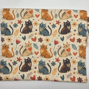 May include: A rectangular fabric pouch featuring a repeating pattern of orange and gray cats with heart-shaped markings on their chests, interspersed with small flowers, leaves, and heart shapes on a cream-colored background with quilted stitching.