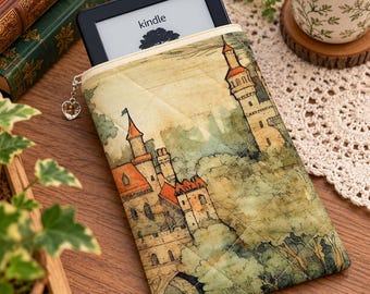May include: A quilted fabric e-reader sleeve featuring a printed illustration of a castle with orange roofs surrounded by green trees. The sleeve has a silver heart-shaped zipper pull and contains a black Kindle e-reader device.
