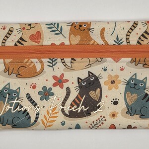 May include: A rectangular fabric notions pouch featuring a cream background with a repeating pattern of cats, hearts, and flowers in shades of orange, gray, and brown. It has an orange zipper closure with a small silver daisy charm and the text Notions Pouch 2.