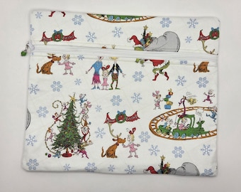 May include: A rectangular quilted zipper pouch featuring a white fabric base with a repeating pattern of Dr. Seuss characters, including a green creature, a dog with antlers, and a decorated Christmas tree, accented by blue snowflakes and text.