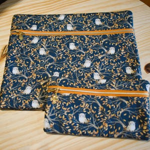 K&ouml;nnte beinhalten: Zwei Rei&szlig;verschlusstaschen mit einem sich wiederholenden Muster aus wei&szlig;en Eulen und goldenen Bl&auml;ttern auf marineblauem Hintergrund. Die Taschen haben orangefarbene Paspeln und goldene Rei&szlig;verschl&uuml;sse.
