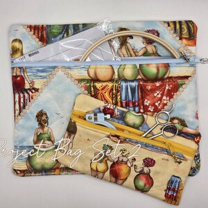 May include: A large quilted project bag with a light blue zipper and a smaller matching pouch with a yellow zipper, both featuring a colorful beach scene print with figures in swimwear. The set includes a wooden embroidery hoop and metal scissors.