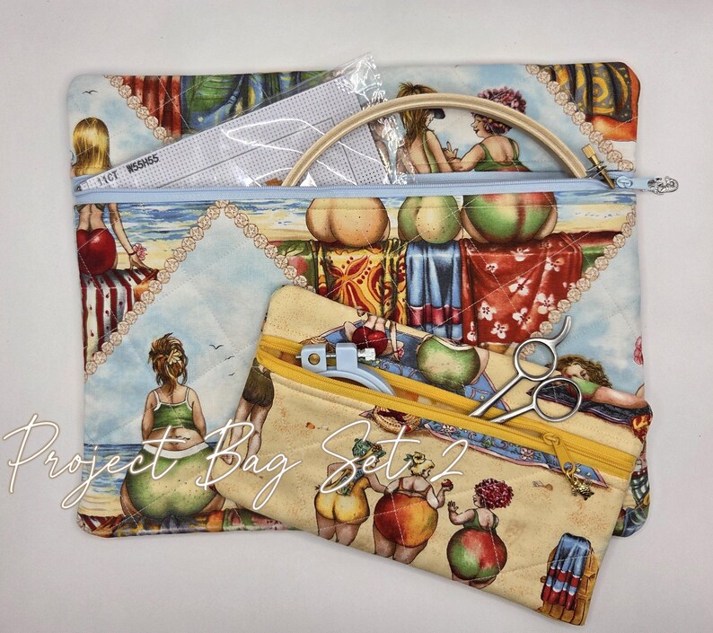 May include: A large quilted project bag with a light blue zipper and a smaller matching pouch with a yellow zipper, both featuring a colorful beach scene print with figures in swimwear. The set includes a wooden embroidery hoop and metal scissors.