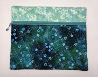 May include: A rectangular fabric zipper pouch featuring a two-tone design. The top section has a light green floral pattern, while the larger bottom section is a dark teal fabric with a grid of thin white lines and small blue flower accents.