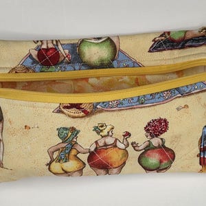 May include: A rectangular quilted fabric pouch featuring a beige background with a repeating print of cartoon figures in swimwear on a beach. The pouch has a yellow zipper closure along the top edge and a small gold-toned metal charm on the zipper pull.