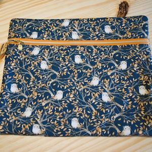 K&ouml;nnte beinhalten: Eine rechteckige, gesteppte Tasche mit marineblauem Hintergrund und einem Muster aus wei&szlig;en Eulen, die in goldbraunen B&auml;umen sitzen. Die Tasche hat einen goldenen Rei&szlig;verschluss mit orangefarbener Paspel und eine kleine, beige Quaste.