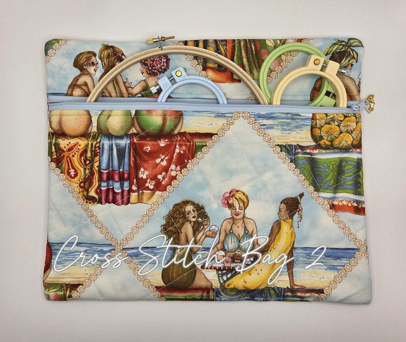 May include: A rectangular quilted fabric bag with a light blue zipper closure, featuring a beach-themed print of people and fruit. Inside the bag are three circular embroidery hoops in light wood, light blue, and light green. Text reads Cross Stitch Bag 2.