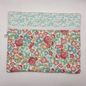 May include: A rectangular zippered pouch featuring a two-part design. The top section has a light blue and white floral pattern, while the larger bottom section displays a dense print of red roses, yellow blossoms, and blue flowers on white.