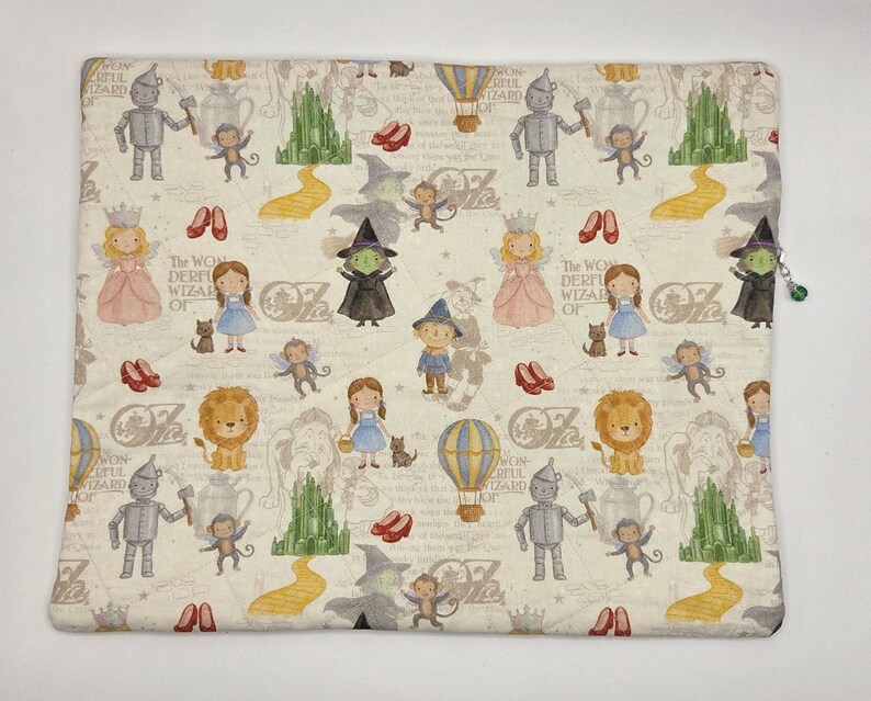 Puede incluir: Una bolsa de tela cuadrada con un patr&oacute;n repetitivo de personajes del Mago de Oz, incluyendo a Dorothy, el Hombre de Hojalata, el Le&oacute;n, el Espantap&aacute;jaros, la Bruja, monos voladores, zapatos rojos, globos aerost&aacute;ticos y la Ciudad Esmeralda.