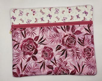 May include: A rectangular zippered pouch featuring a two-tone design. The top section is white with a small pink butterfly pattern. The bottom section displays a dark pink and light pink floral print with palm leaves and a gold butterfly zipper pull.