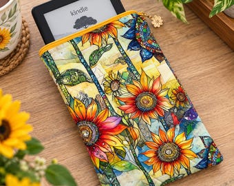May include: A quilted fabric sleeve for an e-reader featuring a vibrant sunflower pattern with stained glass style outlines. The sleeve has a yellow zipper closure with a small flower-shaped metal charm and holds a black Kindle device.