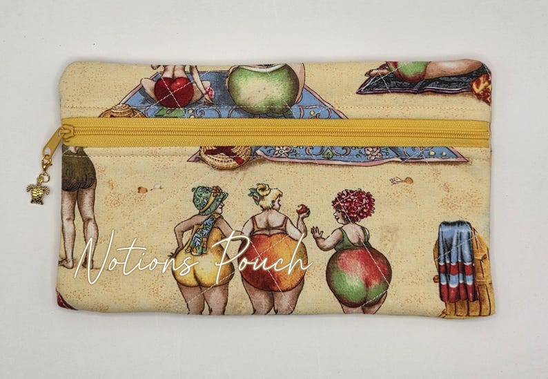 May include: A rectangular fabric pouch with a yellow zipper and a turtle charm. The pouch features a beige background with a repeating print of people in swimwear on a beach. The text "Notions Pouch" is printed in white across the center of the bag.