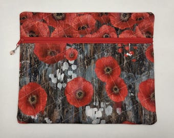 May include: A rectangular zippered pouch featuring a vibrant red poppy floral pattern over a dark, textured background with white accents. The fabric is quilted with a diagonal grid stitch pattern and includes a red zipper closure with a small charm.