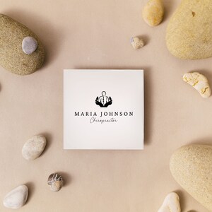 May include: A white business card with a black logo of a person with hands raised above their head. The text "MARIA JOHNSON Chiropractor" is printed below the logo.
