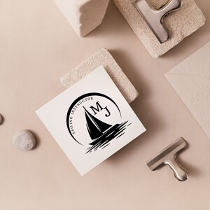 Puede incluir: Un logotipo en blanco y negro con el texto "Sailing Instructor" y las iniciales "M.J." en un c&iacute;rculo. Un velero est&aacute; representado dentro del c&iacute;rculo.