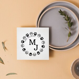 May include: A white card with a black paw print design and the text "Dog Walking" and the initials "M.J." in a circle.
