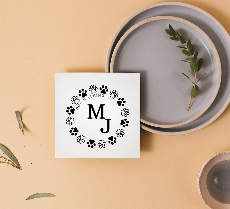 May include: A white card with a black paw print design and the text "Dog Walking" and the initials "M.J." in a circle.