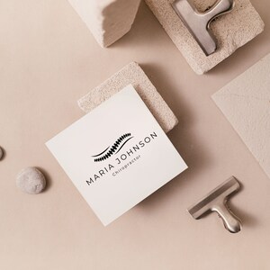 May include: A white business card with black text and a logo of a stylised spine. The text reads "Maria Johnson, Chiropractor".