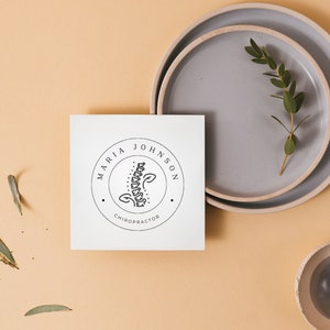 May include: A white card with a black and white logo that says "Maria Johnson, Chiropractor". The logo features a stylised image of a spine.