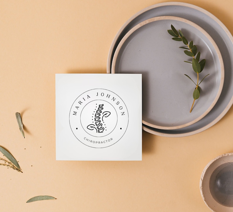 May include: A white card with a black and white logo that says "Maria Johnson, Chiropractor". The logo features a stylised image of a spine.