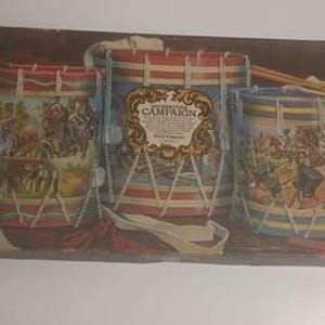 Könnte beinhalten: Vintage-Spieleschachtel mit drei bunten Trommeln mit Illustrationen historischer Schlachten. Die Schachtel ist mit "The American Revolution Campaign Game" beschriftet.