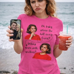 May include: A pink t-shirt with the text "Oh baby, where the hell is my lover? getting down with another?" and images. The person is holding a phone with a photo and a red drink with a straw.