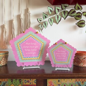 Peut inclure: Deux panneaux décoratifs roses en forme de pentagone avec des bords festonnés et le texte "Quand les choses changent en vous, les choses changent autour de vous". Les panneaux sont sur des supports transparents.