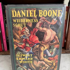 May include: A hardcover book titled "DANIEL BOONE Wilderness Scout" by Stewart Edward White. The cover features a colorful illustration of two men in a fight scene. The book is encased in a clear plastic cover.