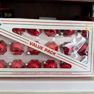 May include: A box of red glass Christmas ornaments. The box is white with red and green trim and the word "Holly" in script. The box reads "Value Pack" and contains 18 ornaments, each 1.25 inches in diameter.