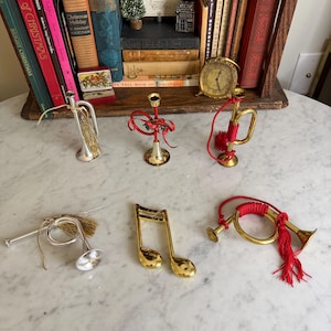 May include: A collection of Christmas ornaments, including miniature trumpets, a musical note, and a candlestick holder. The ornaments are gold and silver, with red accents. A shelf of books is in the background.