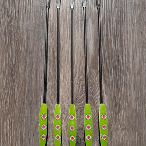 Può includere: Set di cinque forchette da cocktail vintage. Ogni forchetta ha un lungo e sottile stelo in metallo nero e un manico verde. I manici sono decorati con margherite bianche con centri rossi.