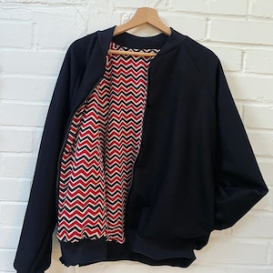 May include: A black bomber jacket with a red, white and black chevron pattern lining. The jacket has a zip closure and a ribbed collar, cuffs and hem.