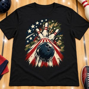 May include: A black short-sleeve t-shirt featuring a graphic print of a dark bowling ball striking three white bowling pins. The design incorporates a patriotic theme with white stars, red stripes, and green camouflage patterns in the background.
