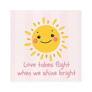 May include: A square, pink background with vertical stripes features a smiling yellow sun with rosy cheeks. The text "Love takes flight when we shine bright" is written in pink cursive font.