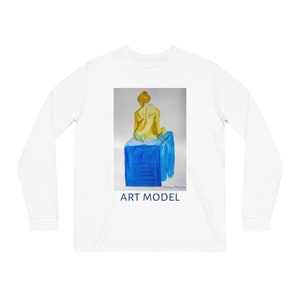 May include: White long-sleeve shirt featuring a watercolor painting of an art model on a blue cube. The painting depicts a figure with yellow skin and hair. The words "ART MODEL" are printed in blue below the painting.
