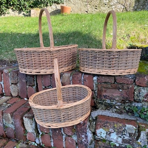 May include: Three brown wicker baskets with handles. The baskets are oval shaped and are sitting on a brick wall.