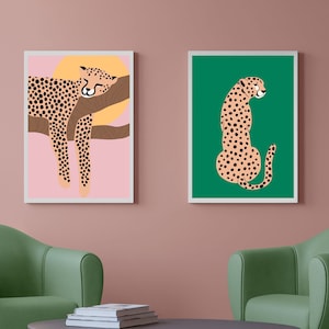 May include: Two framed illustrations of cheetahs. The first illustration shows a cheetah sleeping on a branch with a yellow sun behind it. The background is pink. The second illustration shows a cheetah sitting on a green background.