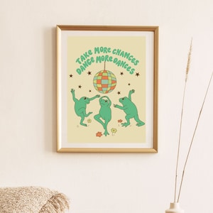 May include: A framed print with a yellow background featuring three green frogs dancing under a disco ball with the text "Take More Chances Dance More Dances".