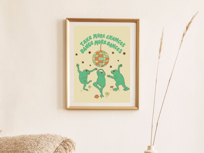 May include: A framed print with a yellow background featuring three green frogs dancing under a disco ball with the text "Take More Chances Dance More Dances".