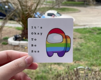 May include: A white sticker with a rainbow-colored Among Us character and the text "It's Okay To Be Sus".