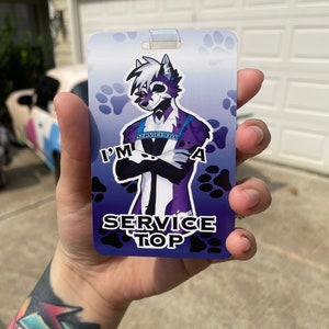 Puede incluir: Una insignia púrpura y azul con un zorro de dibujos animados que lleva un esmoquin negro y un collar que dice "Service Fox". La insignia tiene huellas de patas negras sobre un fondo azul y el texto "I'm a Service Top".
