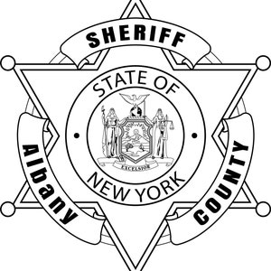 Op de afbeelding: Zwart-witte illustratie van een sheriffster-badge met de tekst "SHERIFF STATE OF NEW YORK ALBANY COUNTY".