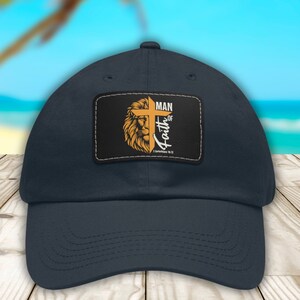 May include: A navy blue baseball cap with a patch featuring a lion's head, a cross, and the text "Man of Faith" with a Bible verse reference.
