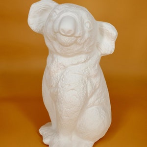 May include: White ceramic koala figurine with a textured surface. The koala is sitting upright with its arms crossed and has a friendly expression.